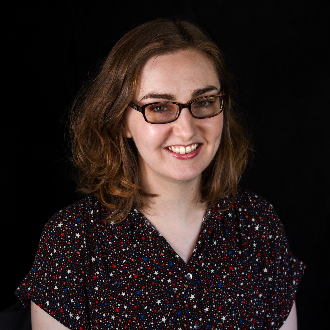 Headshot of Sarah Hughes wearing glasses in front of black backdrop.